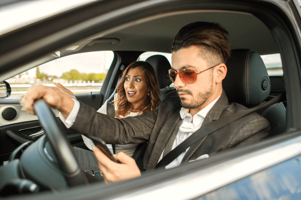 Man texting and driving while a passenger is watching