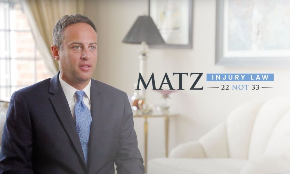 Professional man in suit at Matz Injury Law office. Text: 22 NOT 33. Elegant interior.