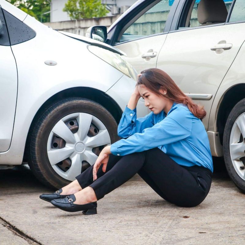 a woman sitting on the ground next to a parked car