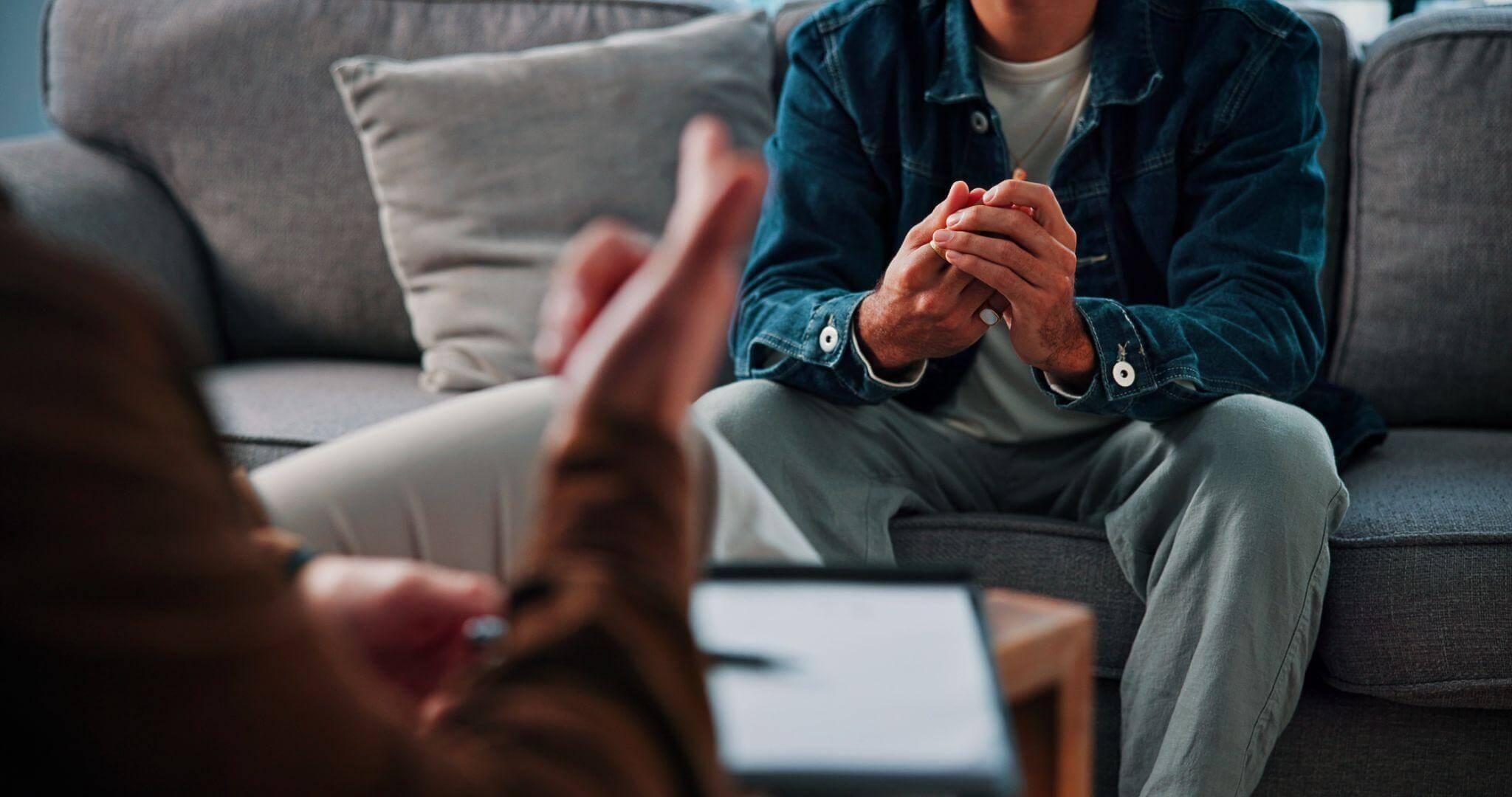 Man sitting on a couch, hands clas