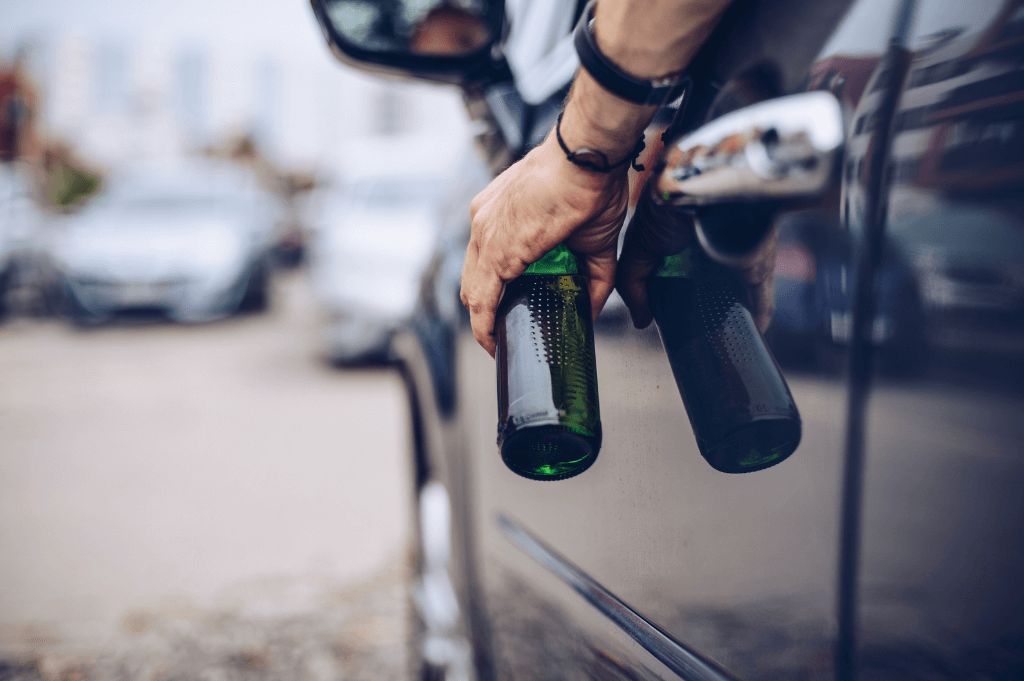 man holding a beer in driver seat of vehicle.