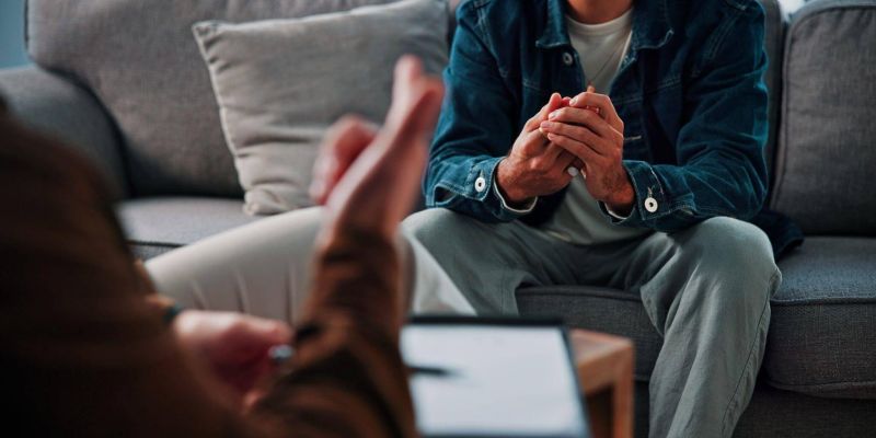 Man sitting on a couch, hands clas