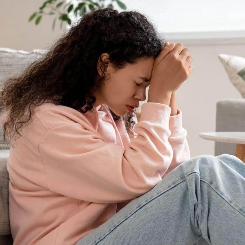 Woman on couch holding her head,