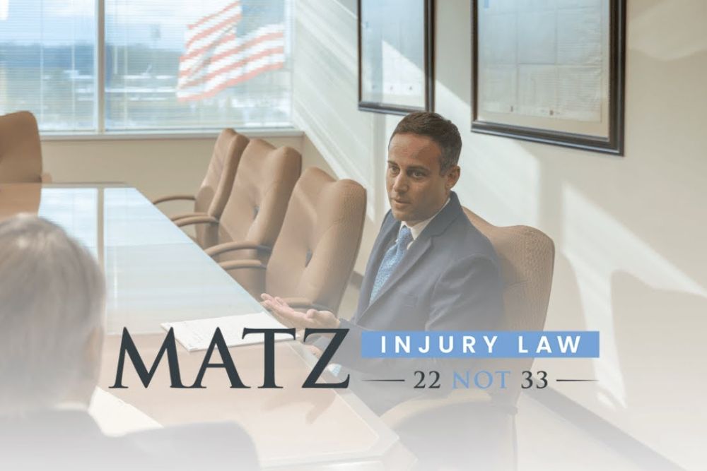 Lawyer in office meeting at Matz Injury Law, discussing legal matters, with window view and company logo displayed.