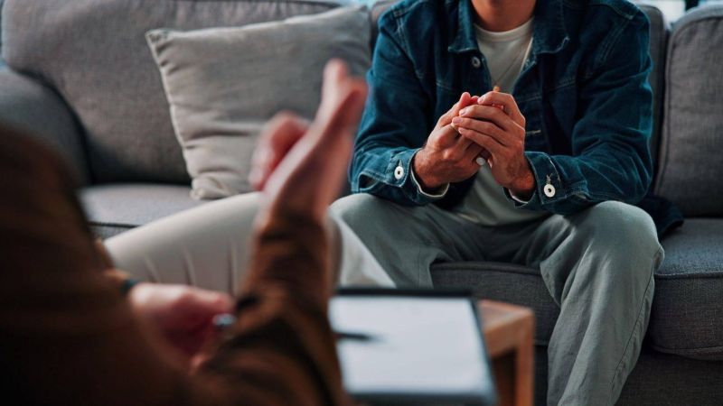 Man sitting on a couch, hands clas