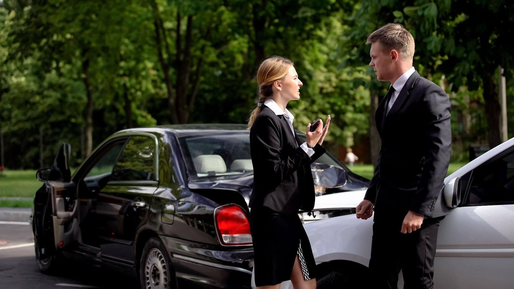 a man and a woman standing in front of two crashed cars, they are arguing