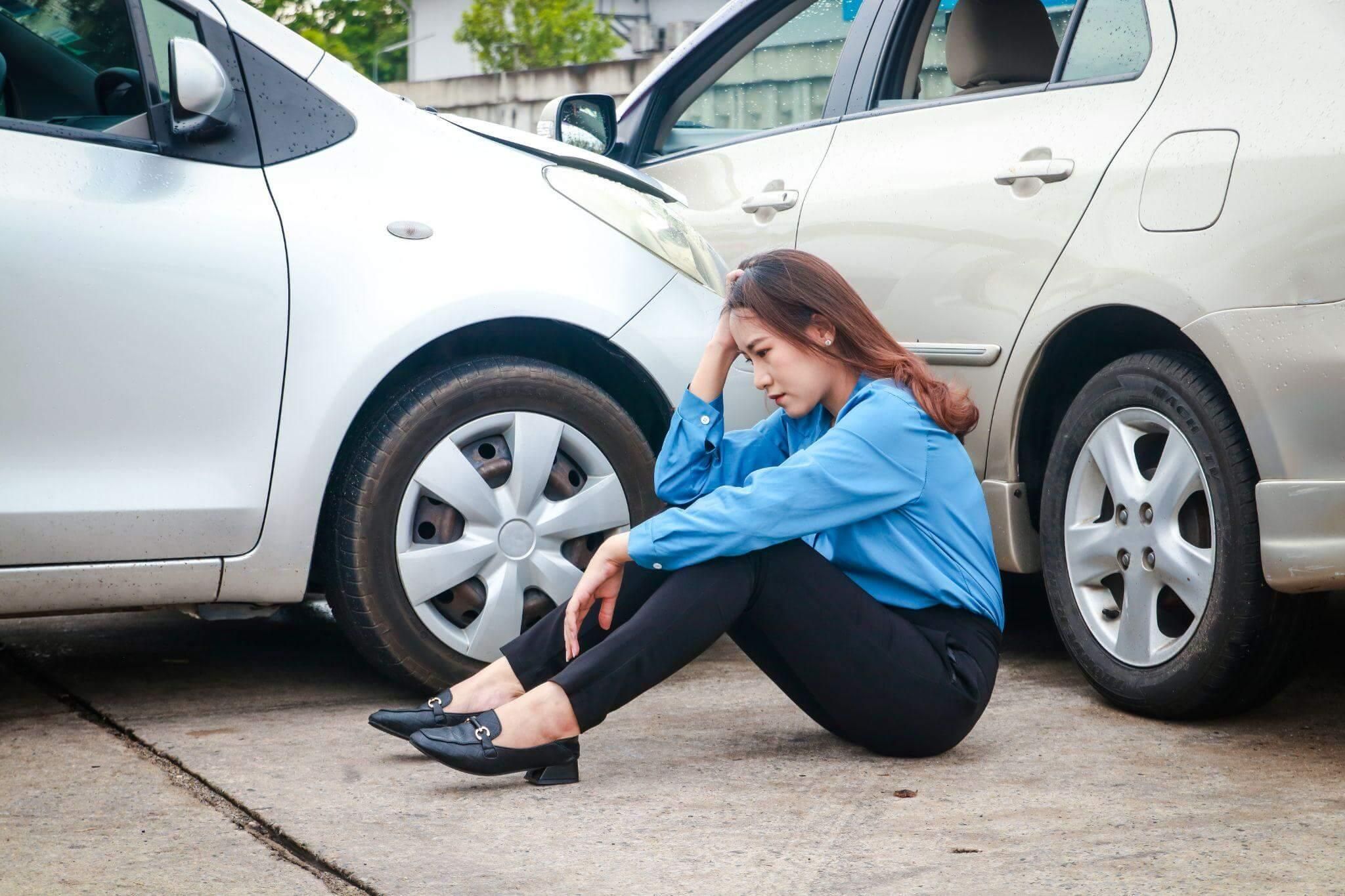 a woman sitting on the ground next to a parked car