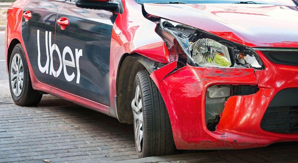 the front of a red car with the word Uber written on it, the car seems to have crashed recently