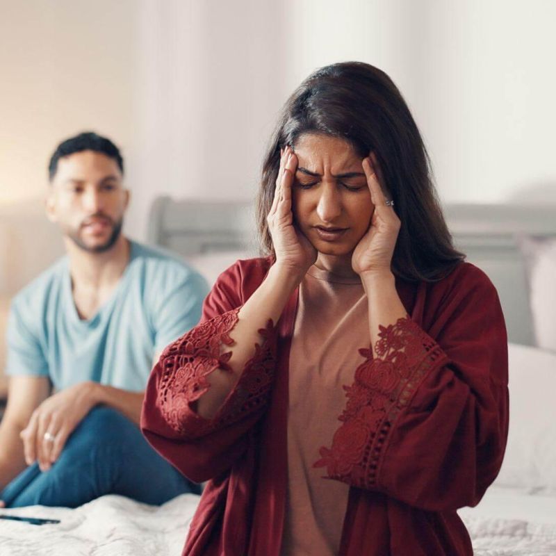 a man and a woman sitting on a bed, she seems to be in distress