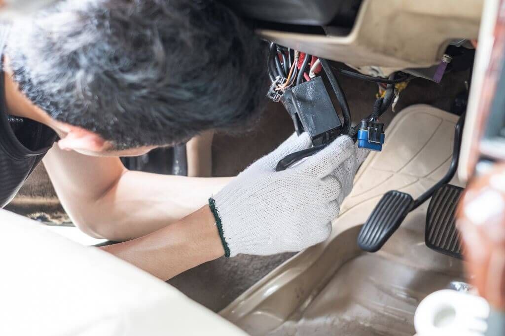 Mechanic with gloves repairing car wiring under dashboard.
