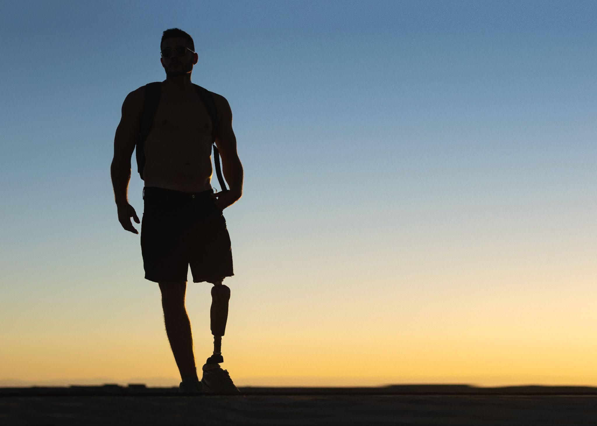 a man walking towards the sun setting down, he has a prosthetic leg
