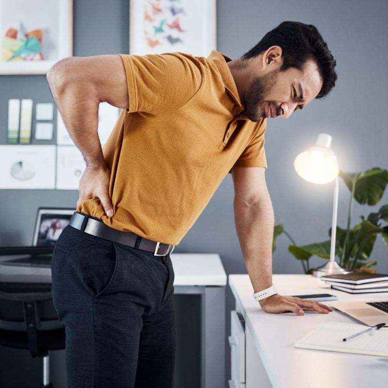 Man in office experiencing back pain while leaning on desk.