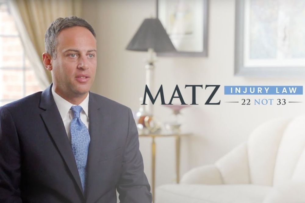 Professional man in suit at Matz Injury Law office. Text: 22 NOT 33. Elegant interior.