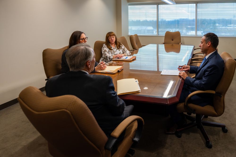 Business meeting in a conference room with four people discussing documents around a table.