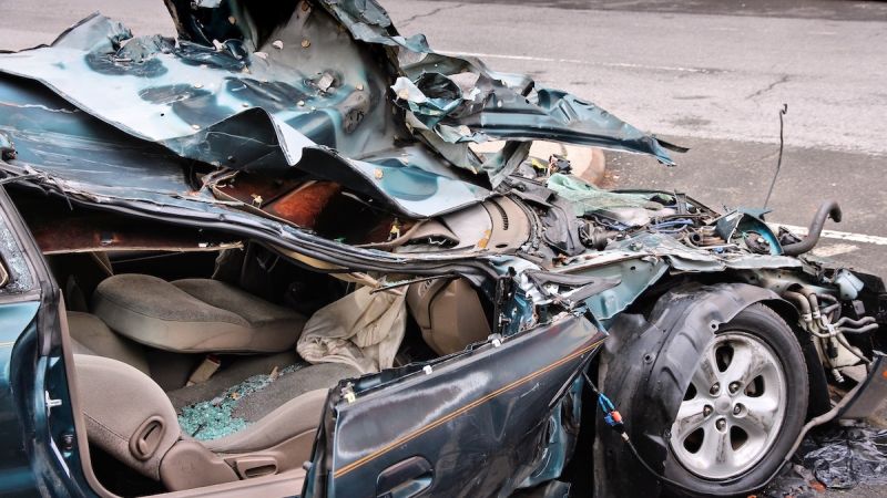 Crashed car with severe damage on street, highlighting road safety and collision impact risks.