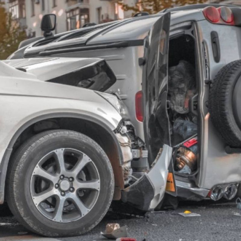Car accident scene with SUV flipped on its side after collision, showing significant vehicle damage on city street.