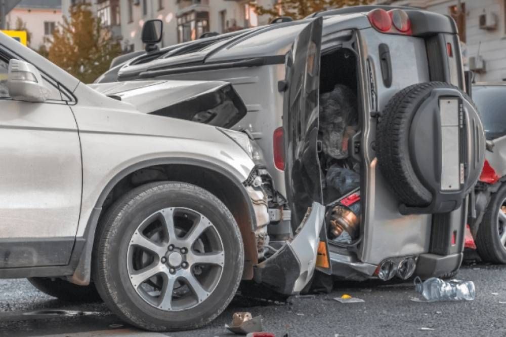 Car accident scene with SUV flipped on its side after collision, showing significant vehicle damage on city street.