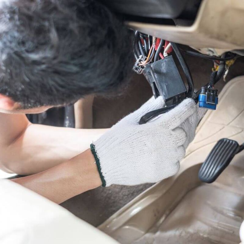 Mechanic with gloves repairing car wiring under dashboard.