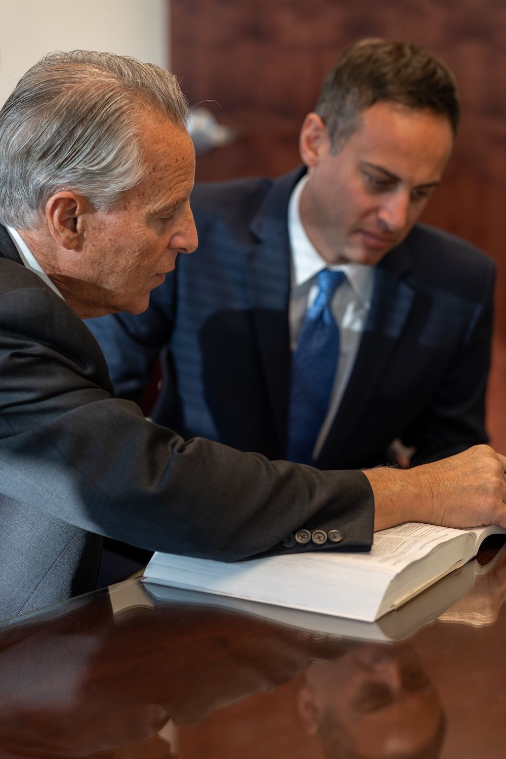 Two businessmen in suits discussing over an open book at a conference table.