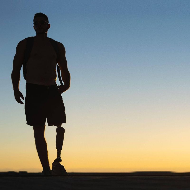 a man walking towards the sun setting down, he has a prosthetic leg