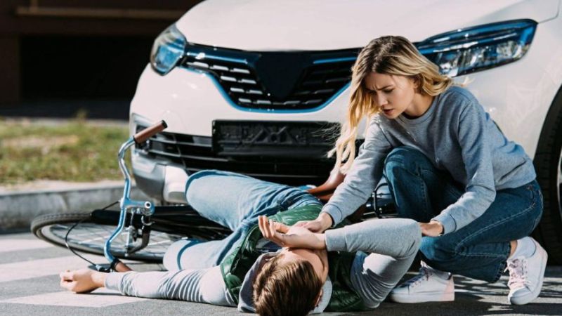 Woman aids injured cyclist after car accident on crosswalk, highlighting road safety awareness.
