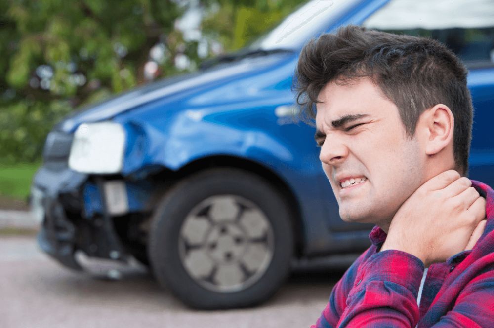 Man holding neck in pain near damaged blue car after accident.