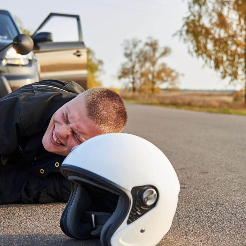 Man lying beside motorcycle helmet on ground, he is in distress and suggests he was just in an accident