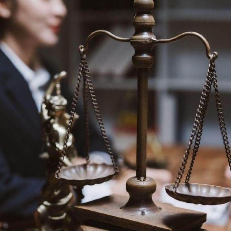 Scale of justice with blurred people discussing law in an office setting.