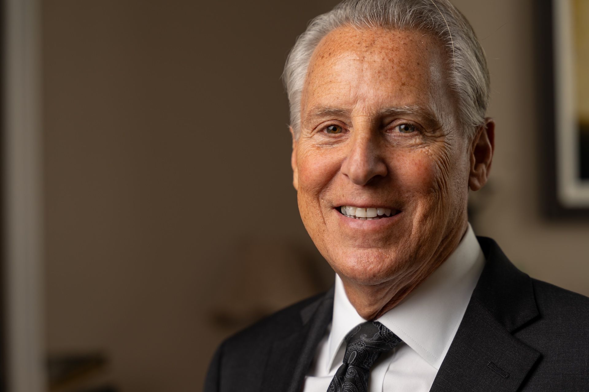 Smiling elderly man in a suit and tie, posing indoors.