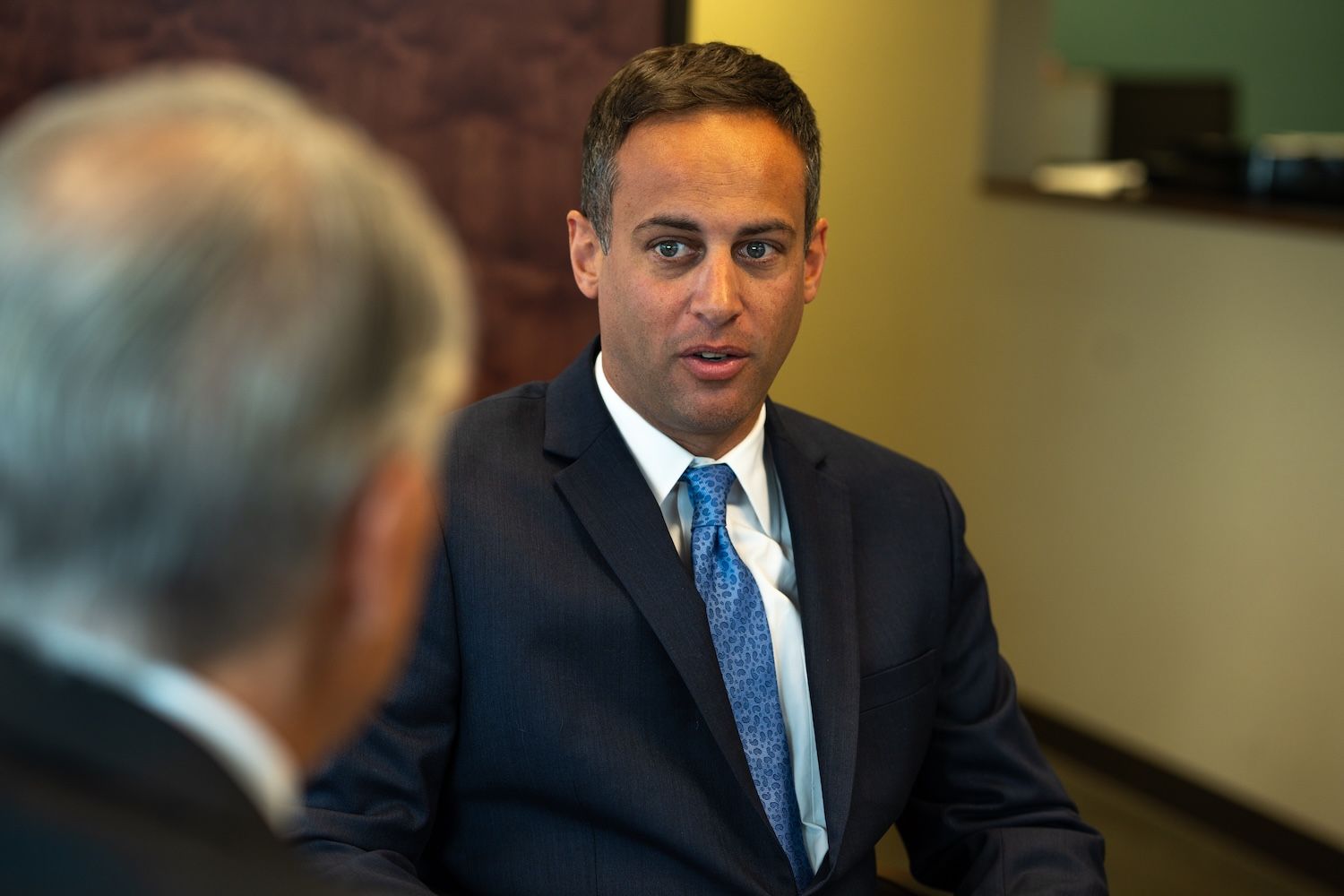 Businessman in a suit with a blue tie having a discussion in an office setting.