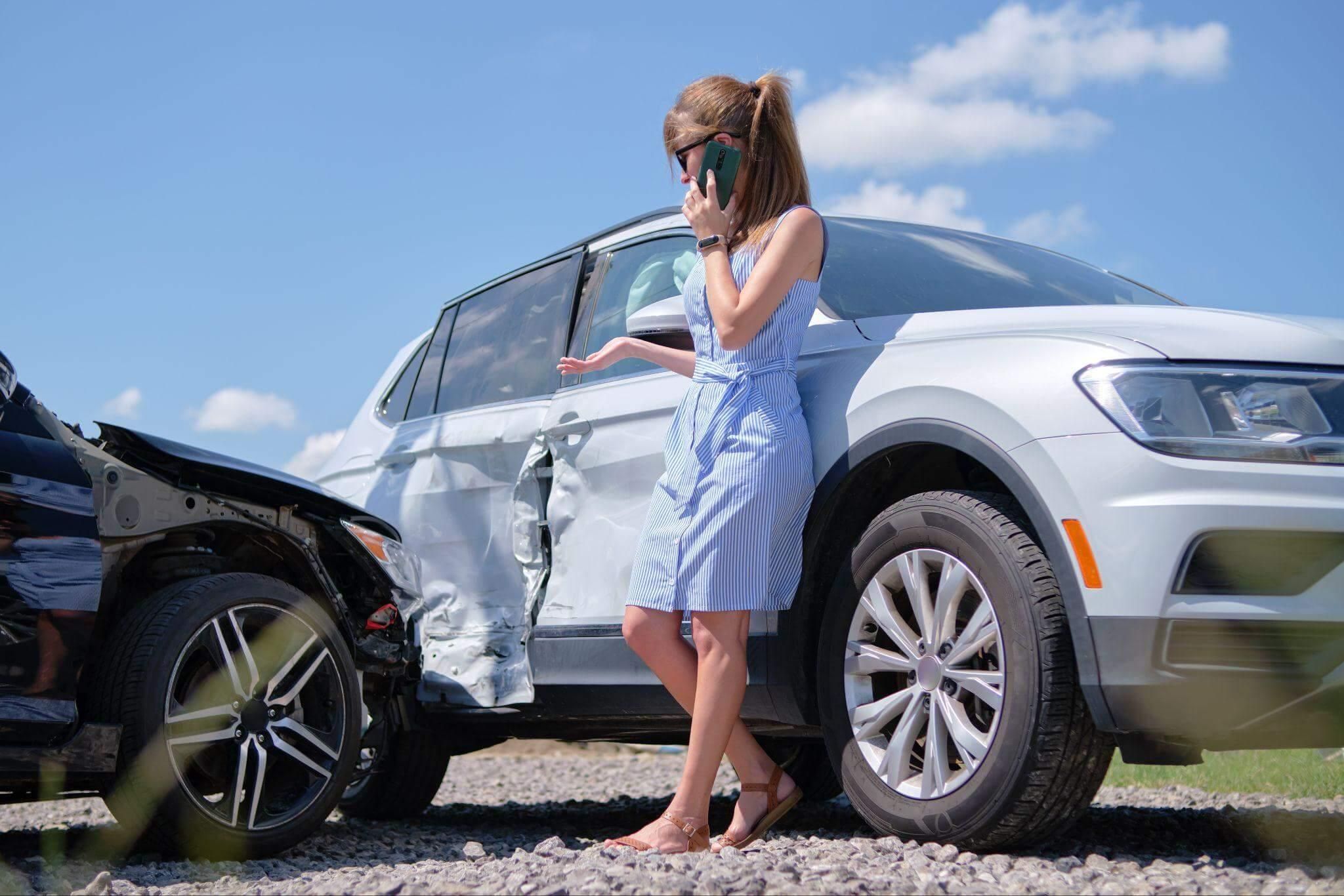 a woman standing next to a white suv that was recently involved in a crash