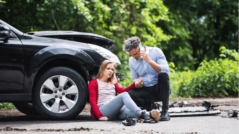 car accident with woman on ground and man holding her hand on the phone