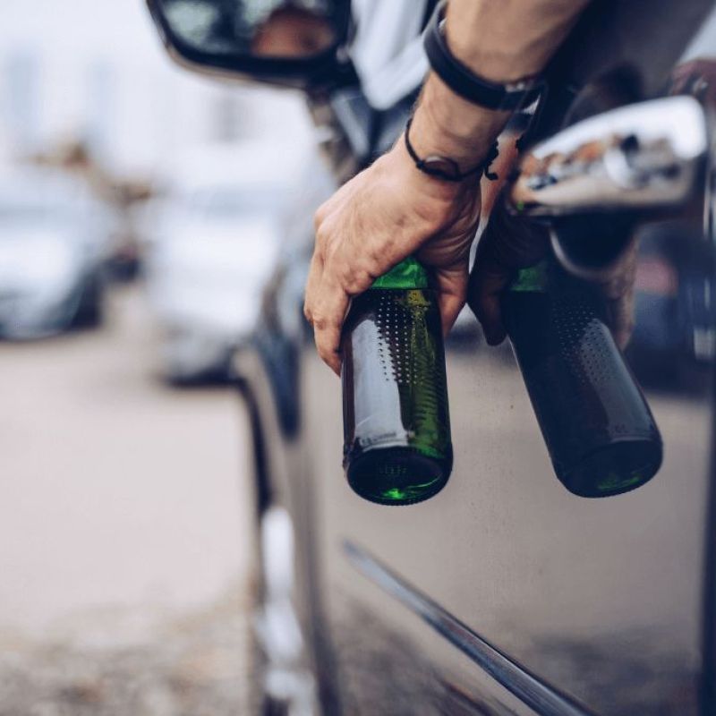 man holding a beer in driver seat of vehicle.