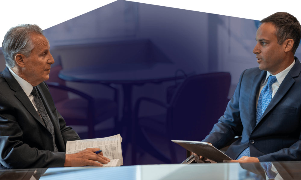 Two businessmen in suits engaged in a meeting, discussing with documents and a tablet in a formal setting.