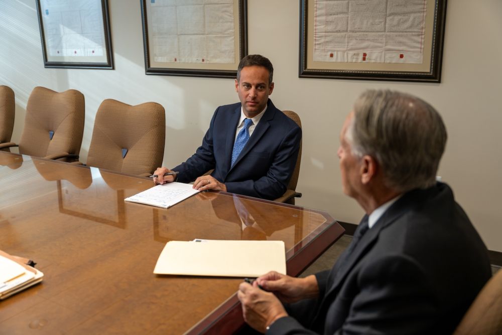 Two businessmen in a conference room, discussing documents at a large wooden table.