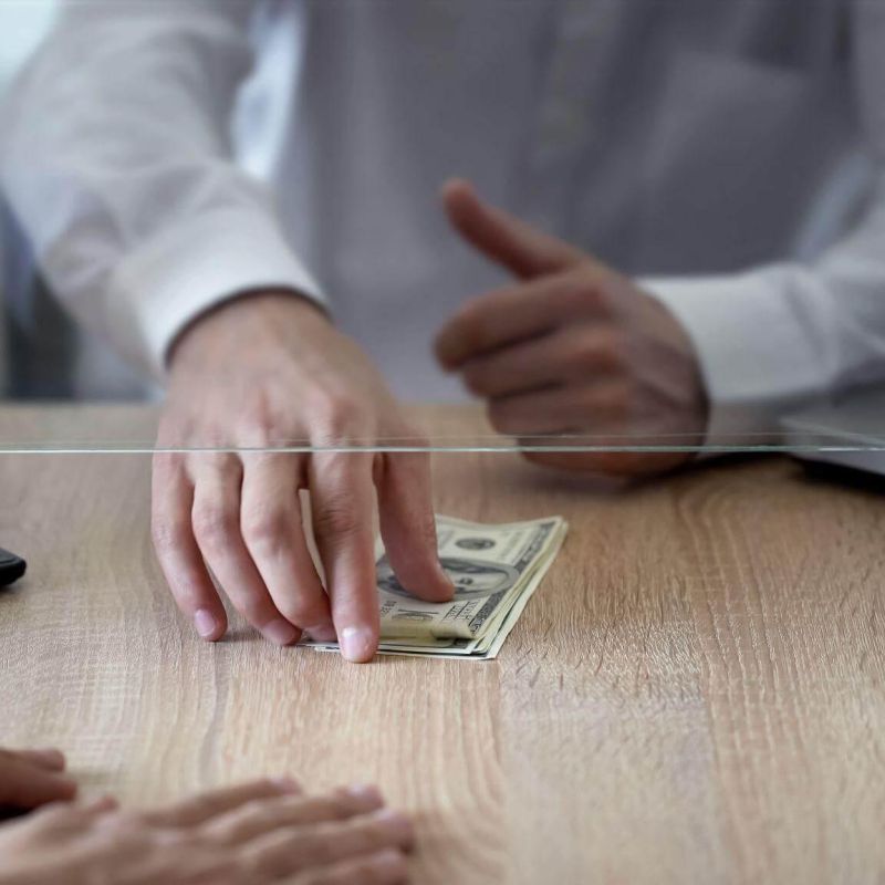 a person sitting at a desk with a stack of money in front of a laptop