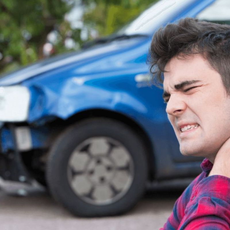 Man holding neck in pain near damaged blue car after accident.