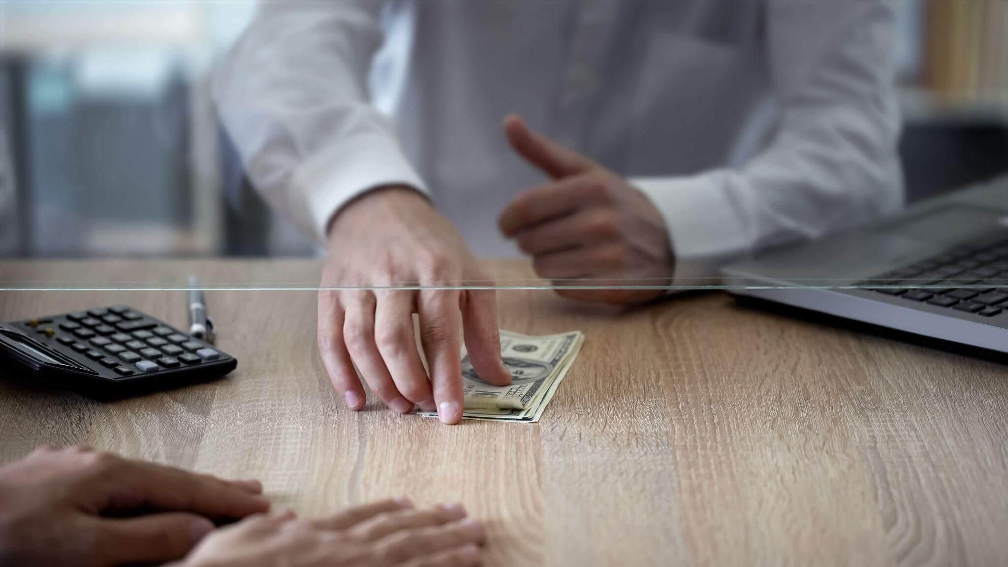 a person sitting at a desk with a stack of money in front of a laptop
