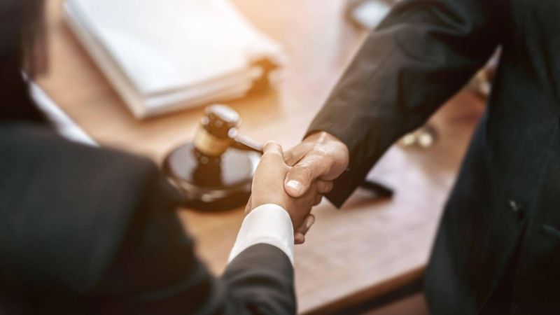 Two people shaking hands over a table after a Michigan