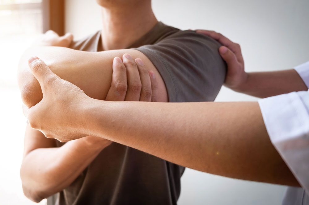 Person receiving physical therapy on shoulder by a therapist.