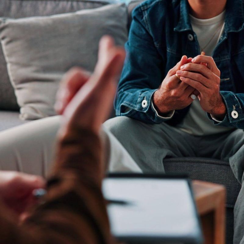 Man sitting on a couch, hands clas