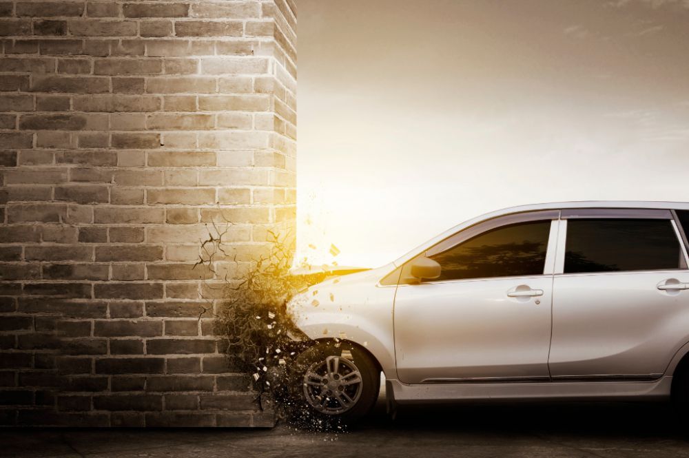 Car crashing into brick wall with debris flying, illustrating impact force and vehicle collision.
