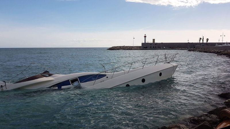 a white boat is in the water near the shore and is slowly sinking