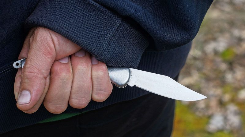 Hand holding a folding knife behind back, close-up view.