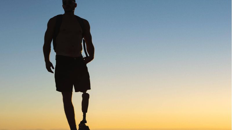 a man walking towards the sun setting down, he has a prosthetic leg