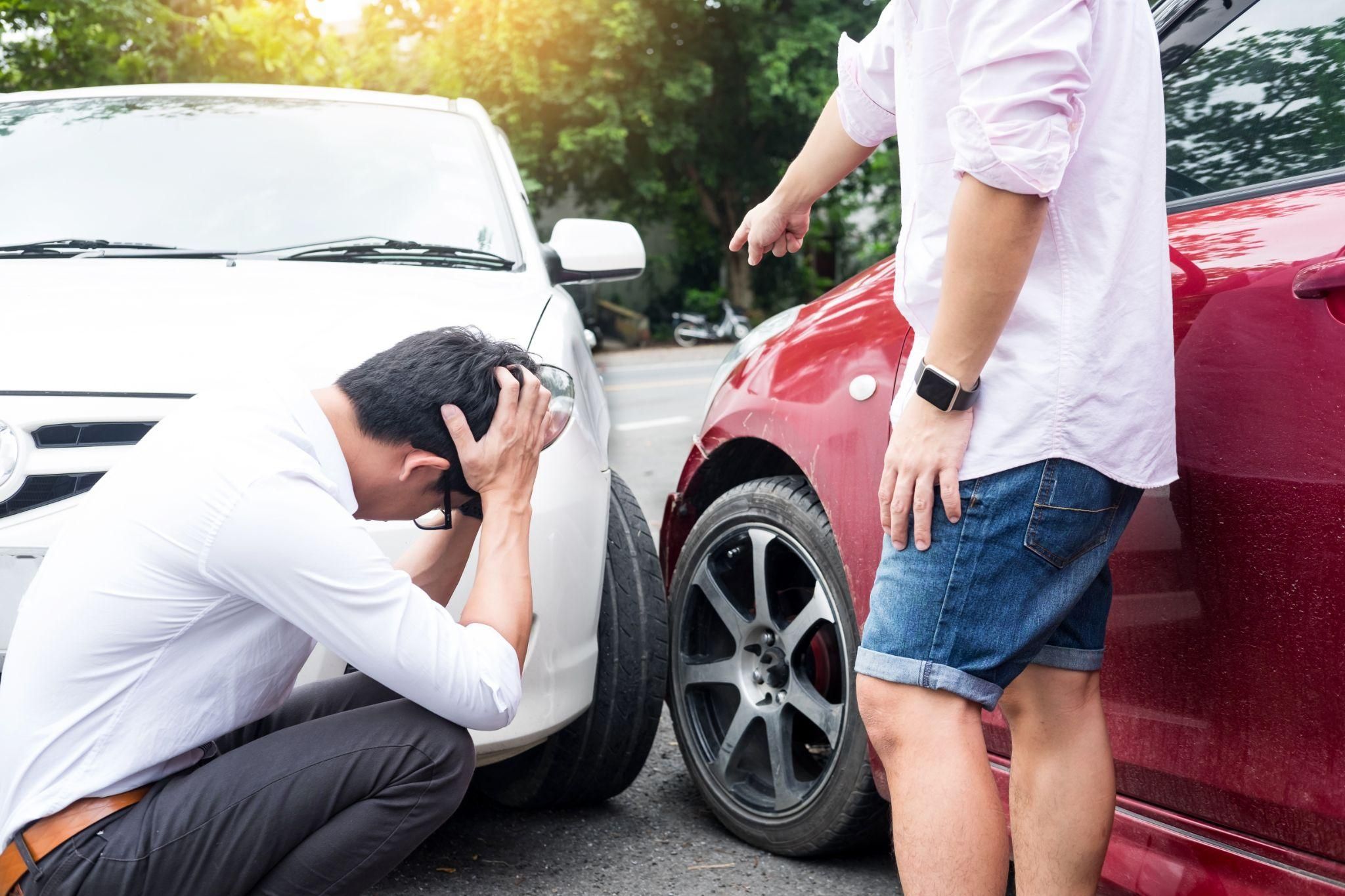 Two cars involved in accident; one person crouching stressed, other standing and pointing at the damage.