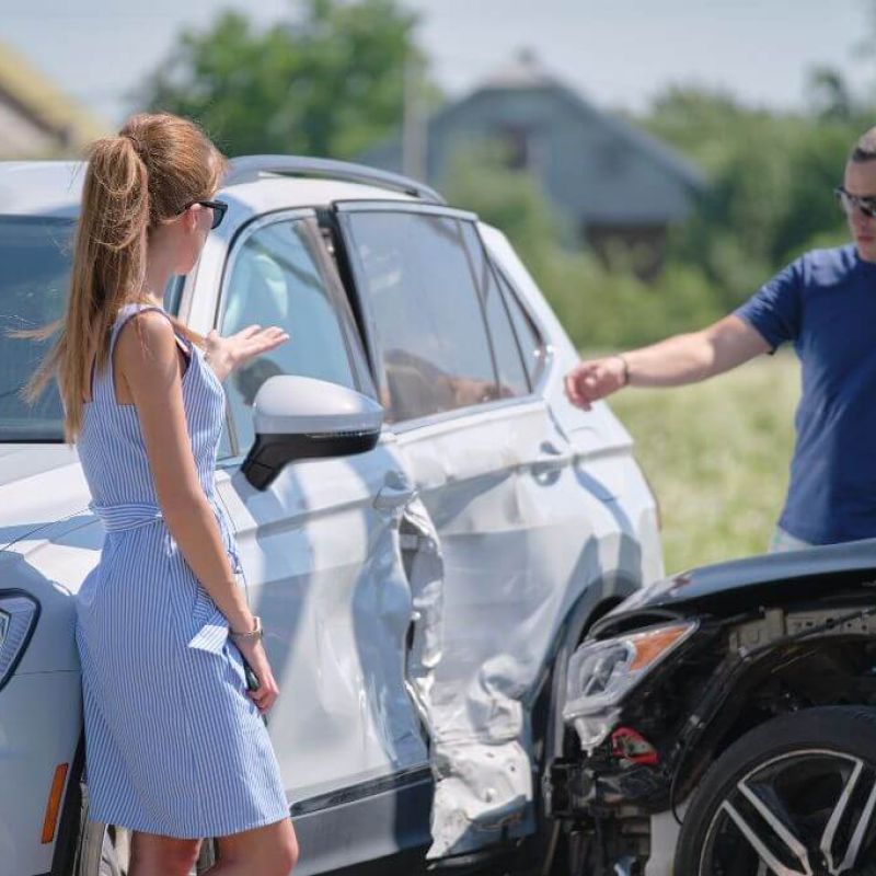 Two people discuss car accident damage on a sunny day.