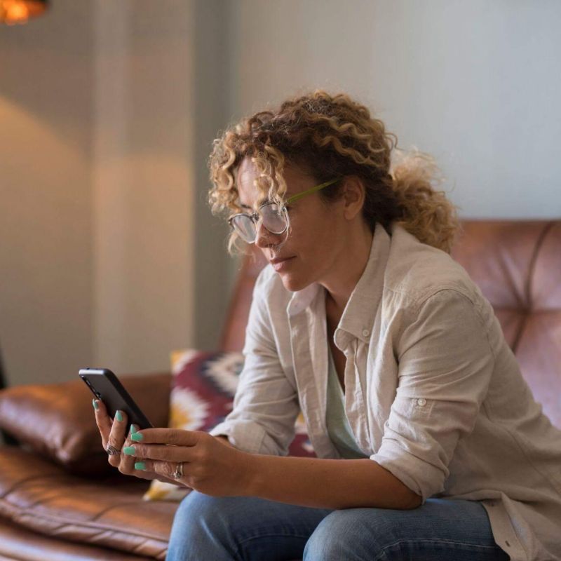 Woman on couch using smartphone, she is visibly worried