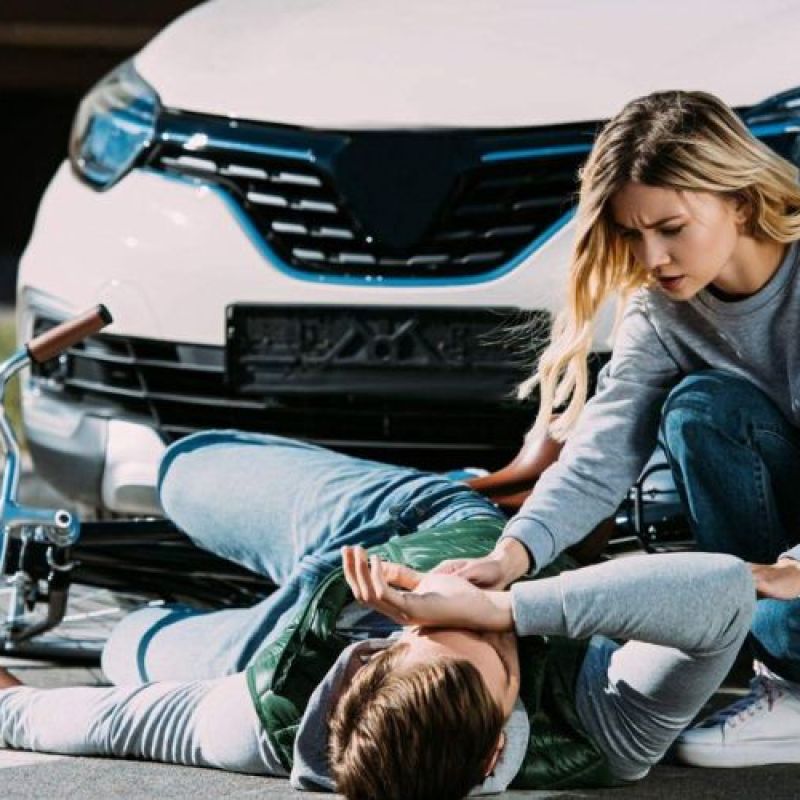 Woman aids injured cyclist after car accident on crosswalk, highlighting road safety awareness.