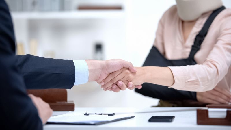 Woman wearing an arm sling shaking hands with a lawyer